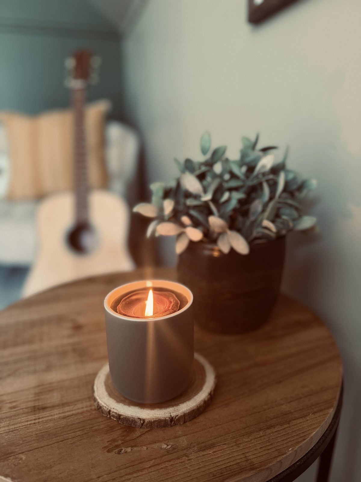 A lit candle and a small potted plant on a wooden side table