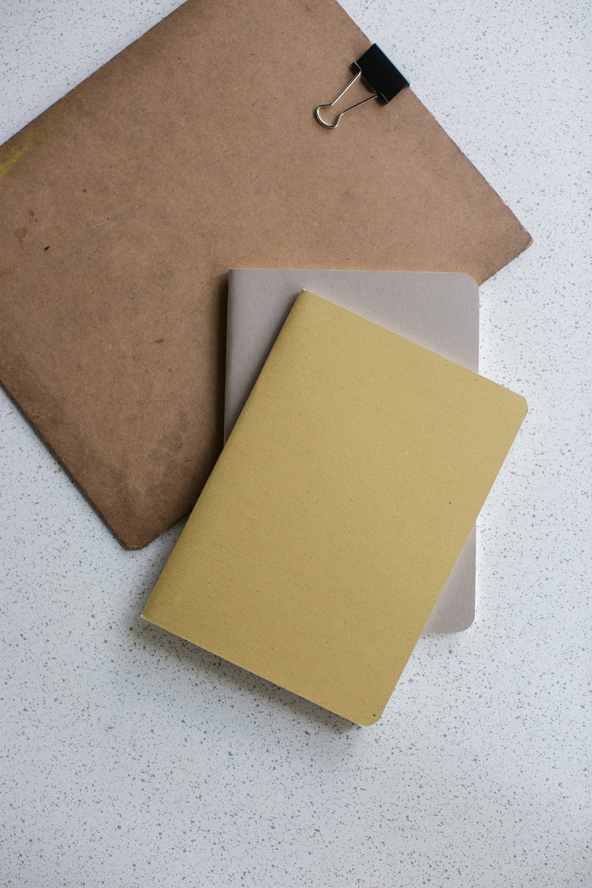 A mustard folder and a grey notebook resting on a kraft paper clipboard